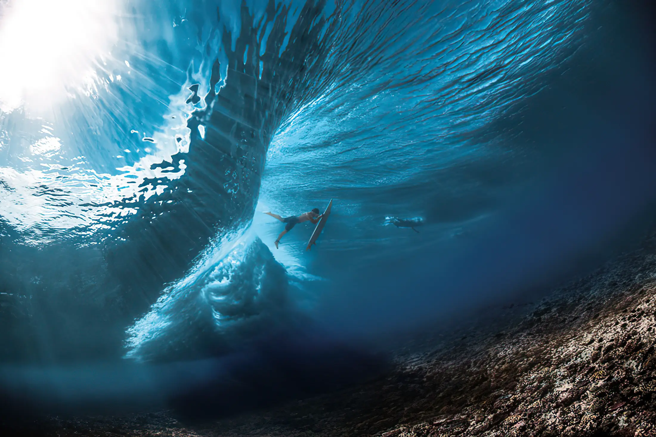 Imagen ilustrativa de un surfista dentro del tubo de una ola, vista submarina